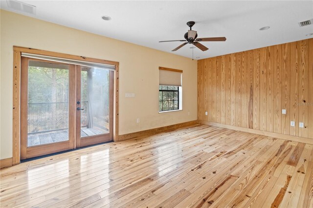 spare room featuring wooden walls, ceiling fan, light hardwood / wood-style floors, and a wealth of natural light