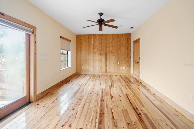 spare room with light wood-type flooring, ceiling fan, and wooden walls