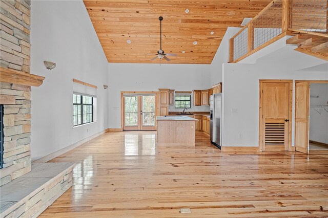 unfurnished living room featuring light hardwood / wood-style floors, wood ceiling, a fireplace, and a high ceiling