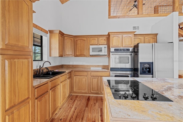 kitchen with a high ceiling, sink, light hardwood / wood-style flooring, light brown cabinetry, and stainless steel appliances