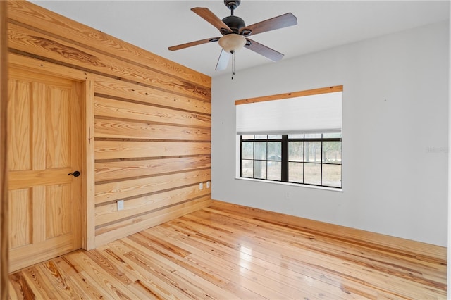 empty room featuring hardwood / wood-style flooring, ceiling fan, and wooden walls