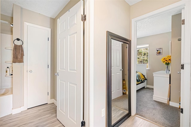 hall with light wood-type flooring and a textured ceiling