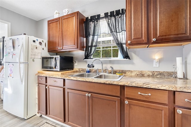 kitchen with sink, light stone counters, light hardwood / wood-style flooring, white refrigerator, and a textured ceiling