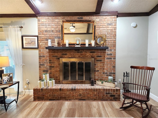 living room with hardwood / wood-style floors, a textured ceiling, a brick fireplace, and ceiling fan