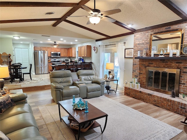 living room with vaulted ceiling with beams, ceiling fan, light hardwood / wood-style floors, and a brick fireplace