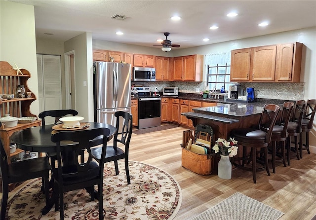 kitchen featuring a breakfast bar, backsplash, light hardwood / wood-style flooring, appliances with stainless steel finishes, and kitchen peninsula