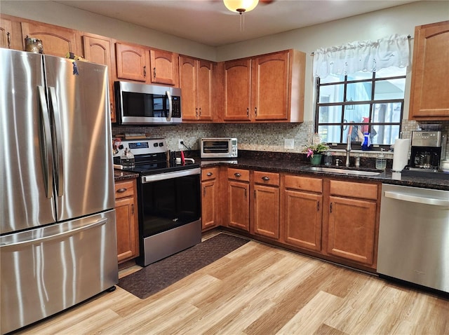 kitchen featuring sink, tasteful backsplash, dark stone counters, light hardwood / wood-style floors, and appliances with stainless steel finishes