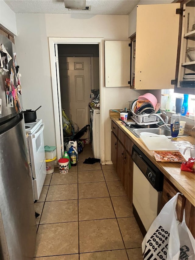 kitchen featuring washing machine and clothes dryer, sink, a textured ceiling, white appliances, and light tile patterned floors