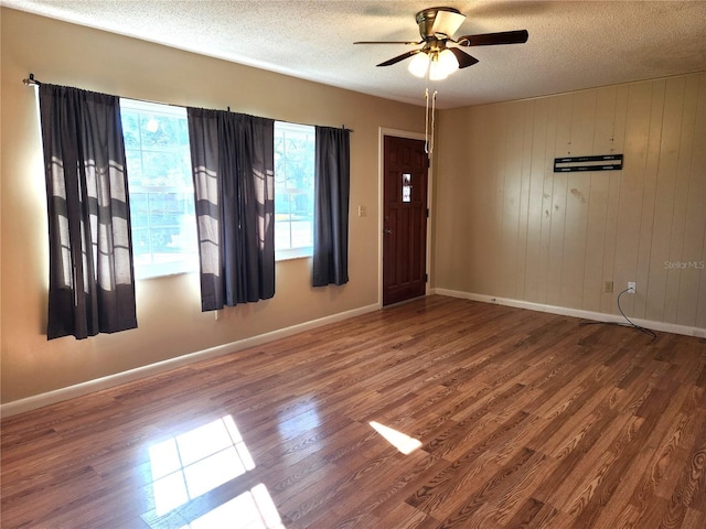 empty room with hardwood / wood-style floors, ceiling fan, a healthy amount of sunlight, and wood walls