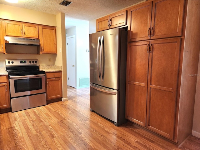 kitchen with a textured ceiling, stainless steel appliances, and light hardwood / wood-style flooring