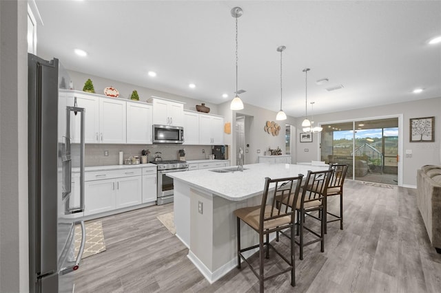 kitchen with pendant lighting, a kitchen island with sink, sink, white cabinetry, and stainless steel appliances