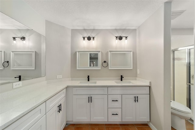 bathroom with vanity, toilet, a shower with shower door, and a textured ceiling