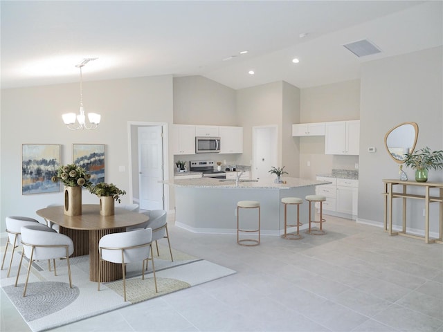 kitchen featuring a kitchen island with sink, stainless steel appliances, light stone counters, white cabinets, and decorative light fixtures