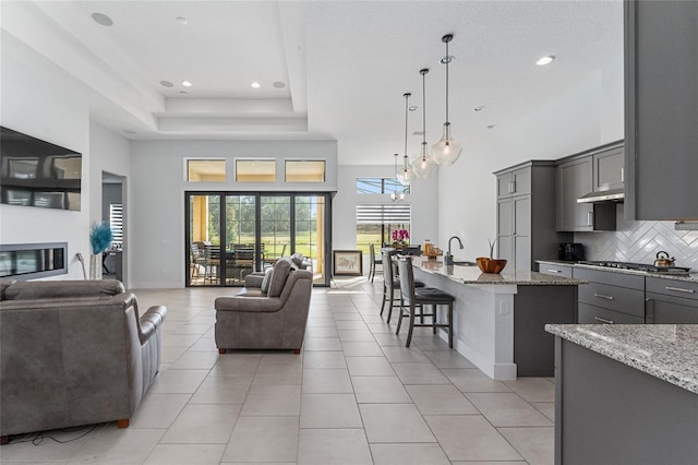 living room featuring a raised ceiling, light tile patterned flooring, a towering ceiling, and sink