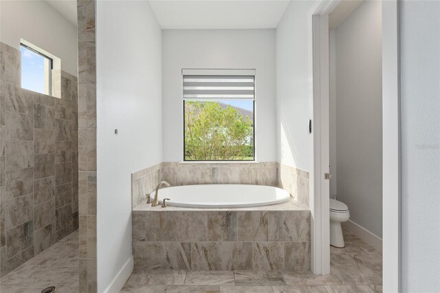 bathroom with plenty of natural light, tiled bath, and toilet