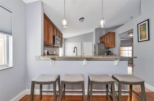 kitchen with lofted ceiling, hanging light fixtures, stainless steel appliances, and a kitchen breakfast bar