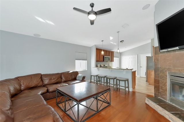 living room with ceiling fan, lofted ceiling, a fireplace, and light wood-type flooring