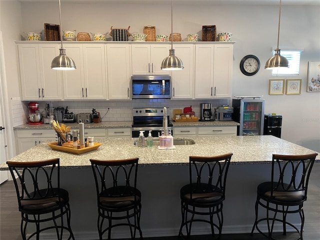 kitchen with a center island with sink, sink, dark hardwood / wood-style floors, white cabinetry, and stainless steel appliances