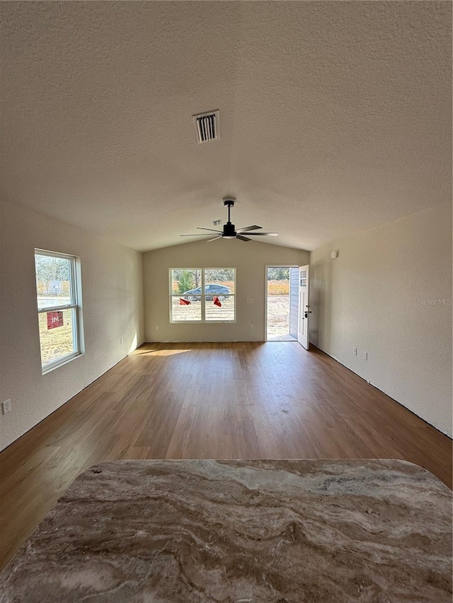 unfurnished living room featuring lofted ceiling, ceiling fan, a textured ceiling, and hardwood / wood-style flooring