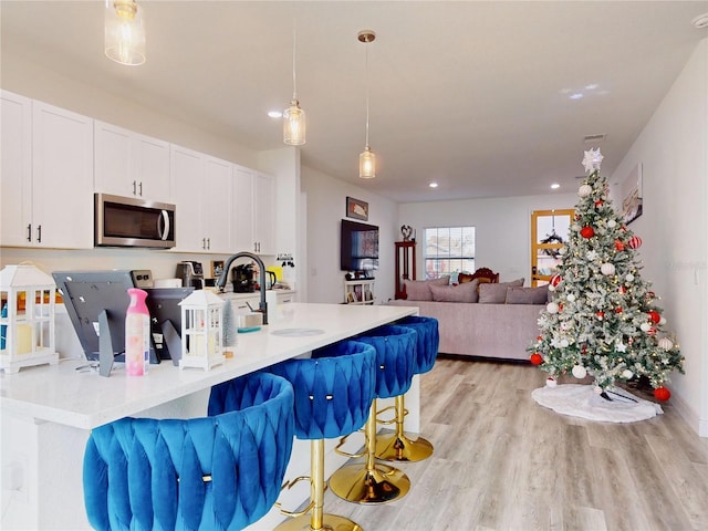 kitchen featuring a breakfast bar, white cabinetry, light hardwood / wood-style flooring, and hanging light fixtures