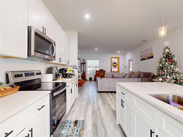 kitchen featuring light stone countertops, white cabinetry, appliances with stainless steel finishes, and light hardwood / wood-style flooring