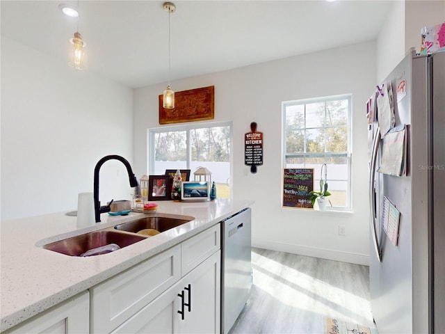 kitchen with appliances with stainless steel finishes, sink, decorative light fixtures, light hardwood / wood-style floors, and white cabinetry