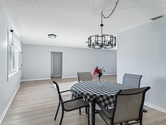 dining space featuring light hardwood / wood-style floors, a textured ceiling, and an inviting chandelier