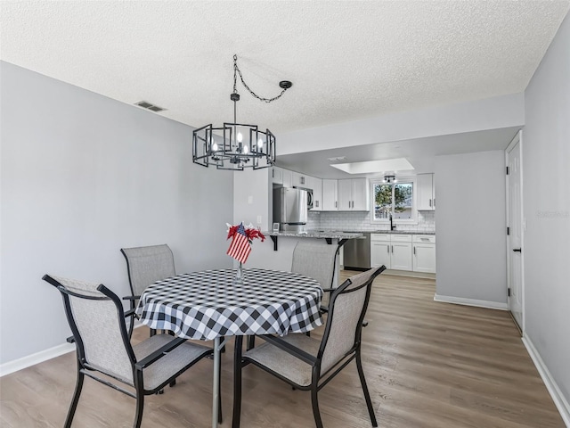 dining area with hardwood / wood-style flooring, a notable chandelier, sink, and a textured ceiling