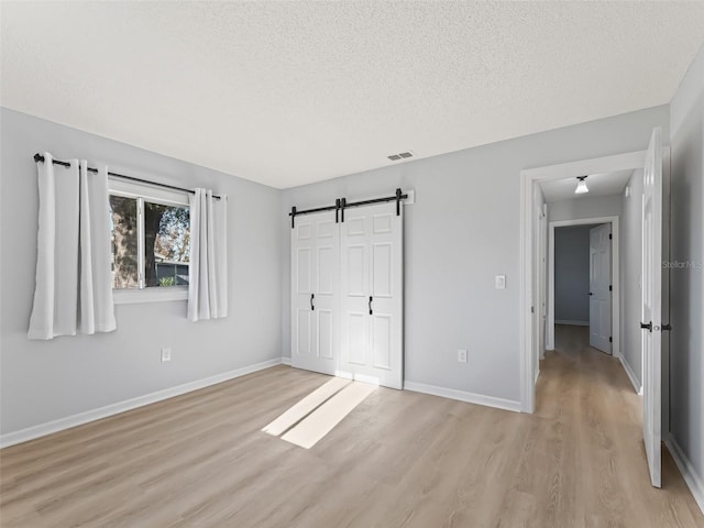 unfurnished bedroom featuring a barn door, light hardwood / wood-style floors, a textured ceiling, and a closet