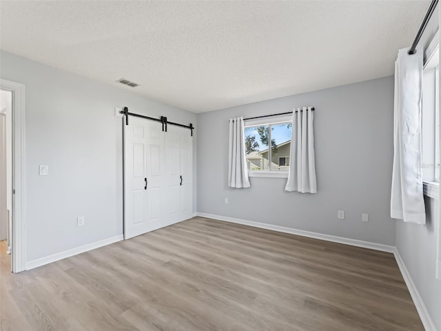 unfurnished bedroom with a textured ceiling, a barn door, and light hardwood / wood-style floors