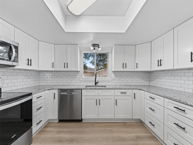 kitchen with stainless steel appliances, white cabinetry, light hardwood / wood-style floors, and sink