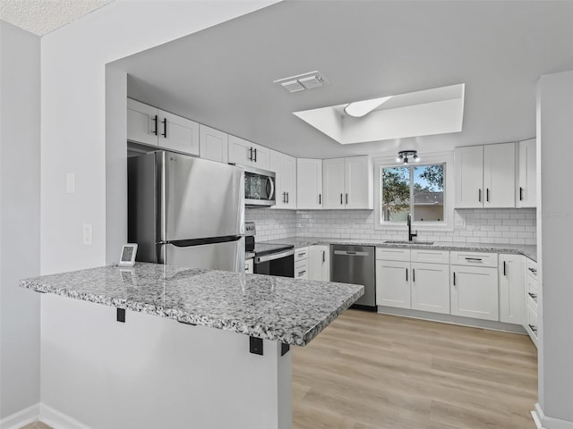 kitchen featuring kitchen peninsula, appliances with stainless steel finishes, sink, light hardwood / wood-style flooring, and white cabinetry