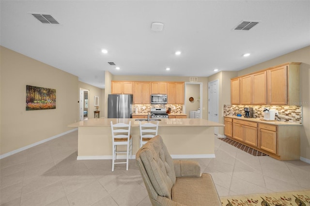 kitchen featuring decorative backsplash, stainless steel appliances, light brown cabinets, light tile patterned floors, and a center island with sink