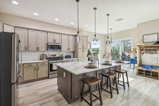 kitchen featuring light hardwood / wood-style floors, a kitchen island with sink, pendant lighting, and appliances with stainless steel finishes