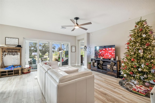 living room featuring ceiling fan, light hardwood / wood-style flooring, and a textured ceiling