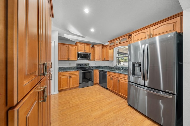 kitchen featuring dark stone counters, stainless steel appliances, vaulted ceiling, sink, and light hardwood / wood-style flooring