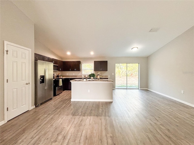 kitchen with dark brown cabinetry, an island with sink, light hardwood / wood-style floors, vaulted ceiling, and appliances with stainless steel finishes