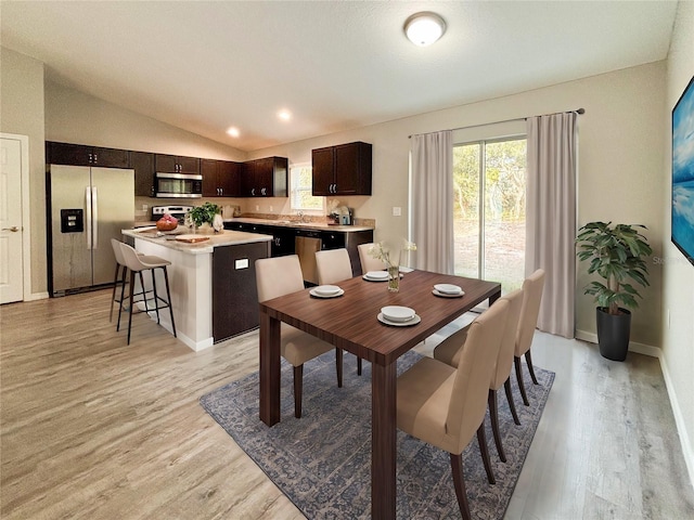 dining room featuring lofted ceiling, sink, and light hardwood / wood-style flooring