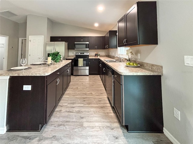 kitchen with a center island, sink, vaulted ceiling, appliances with stainless steel finishes, and light hardwood / wood-style floors