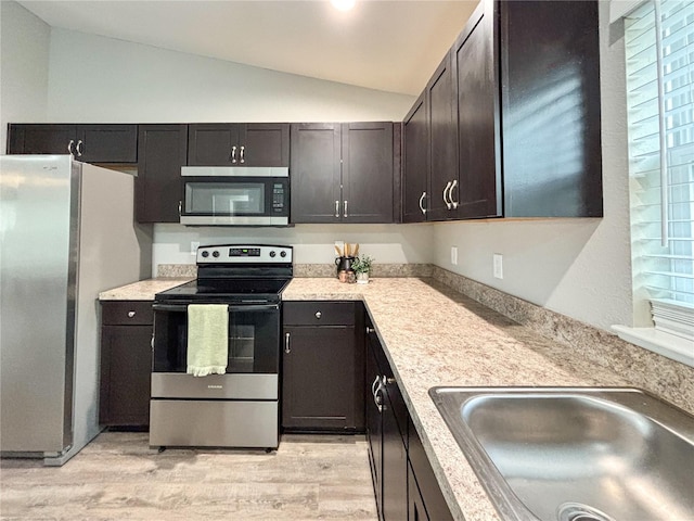 kitchen with stainless steel appliances, a wealth of natural light, lofted ceiling, and light hardwood / wood-style floors