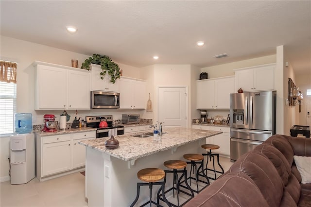 kitchen with a kitchen island with sink, appliances with stainless steel finishes, a kitchen bar, white cabinets, and sink