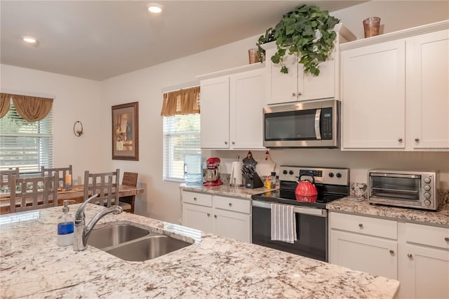 kitchen featuring stainless steel appliances, white cabinets, sink, and light stone countertops