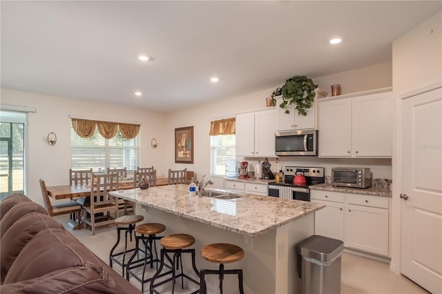 kitchen featuring sink, white cabinets, light stone countertops, a kitchen island with sink, and appliances with stainless steel finishes