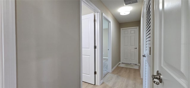 hallway featuring light wood-type flooring, visible vents, a textured ceiling, and baseboards