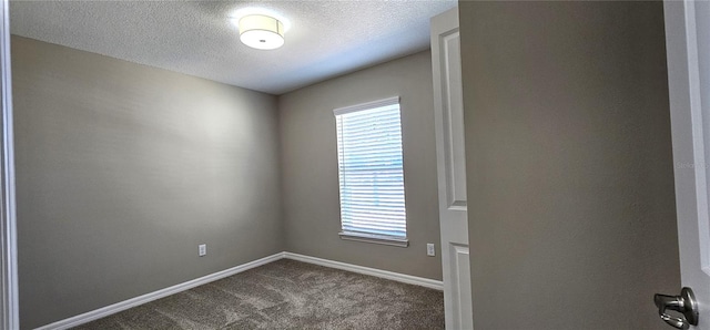 unfurnished room featuring a healthy amount of sunlight, dark carpet, a textured ceiling, and baseboards