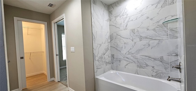 bathroom with a walk in closet, bathing tub / shower combination, visible vents, wood finished floors, and baseboards