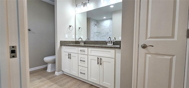 bathroom with double vanity, a shower, toilet, wood finished floors, and a sink