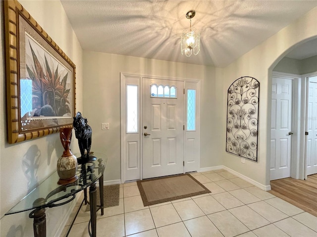 entrance foyer featuring light tile patterned floors, baseboards, arched walkways, and a textured ceiling