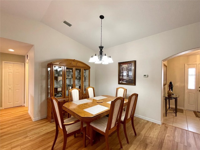 dining room featuring light wood-style floors, visible vents, arched walkways, and vaulted ceiling