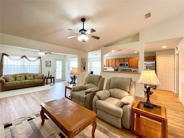 living room with a ceiling fan, lofted ceiling, visible vents, and light wood finished floors